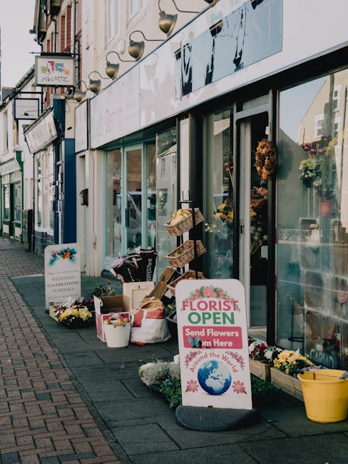 A colorful floral display outside a flower shop on New Malden High Street, featuring a variety of fresh flower arrangements and bouquets. The shop has large glass windows, with potted chrysanthemums a
