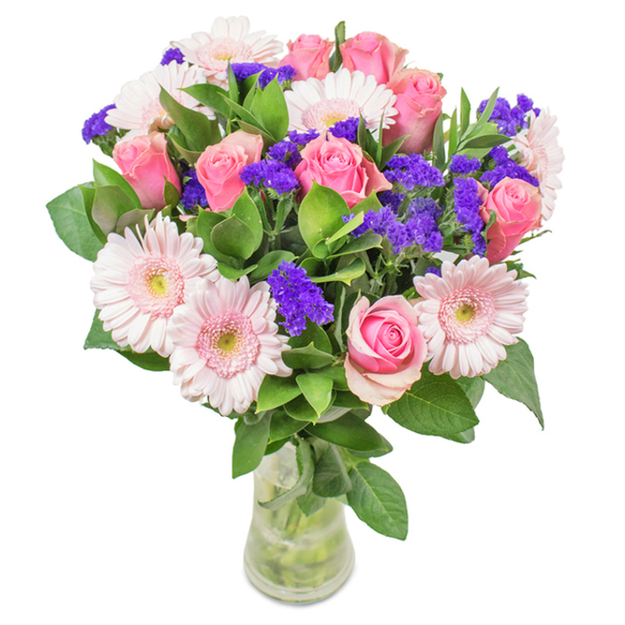 A vibrant and elegantly constructed arrangement stands proudly in a clear glass vase, its freshness unmistakable. In the heart of the bouquet, about seven to nine soft- to mid-toned pink roses are gathered-some still coyly closed, others just beginning to open, their classic spiral shapes a tribute to refined beauty found in New Malden's private gardens. These are encircled by five to seven pale pink gerbera daisies, distinguished by large, round faces and radiating petals, their centers touched with white like morning dew on grass along Kingston Road. Splashes of vivid purple statice or limonium add dimension, offering a lively pop of colour and textural contrast that brings depth much like the vibrant spirit of the local farmers' market. Lush, verdant foliage sets a cooling and abundant base, reminiscent of the greenways winding through the area. The transparent vase-with fresh water visible-completes the natural effect, conjuring the promise of prompt New Malden flower delivery to homes and offices alike. Ideal for birthdays, anniversaries, Mother's Day, or simply delighting someone special, this artful blend of roses, gerberas, and purple accents sends a message of happiness, celebration, and genuine care.